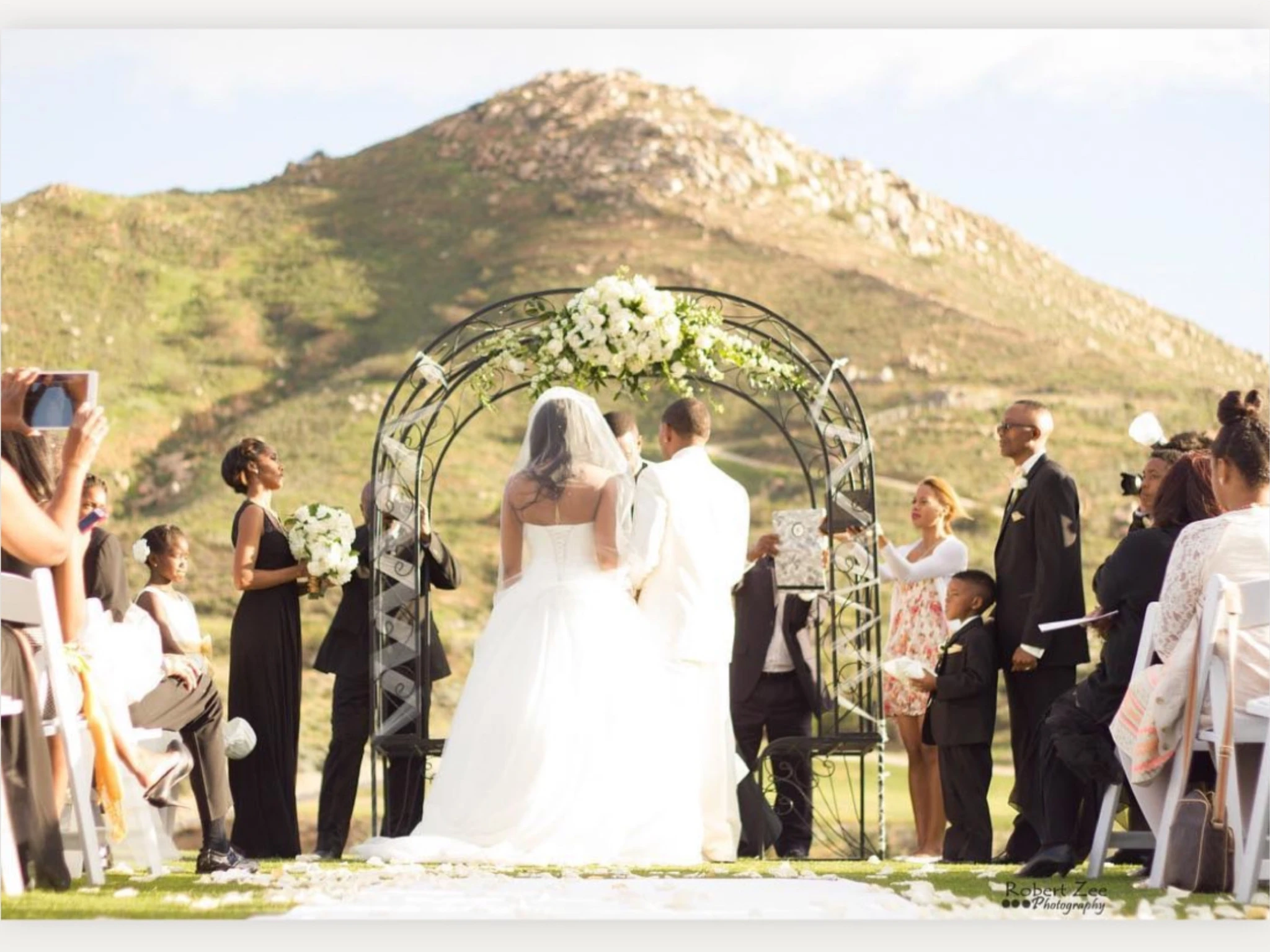 An outdoor wedding ceremony beneath a floral arch
